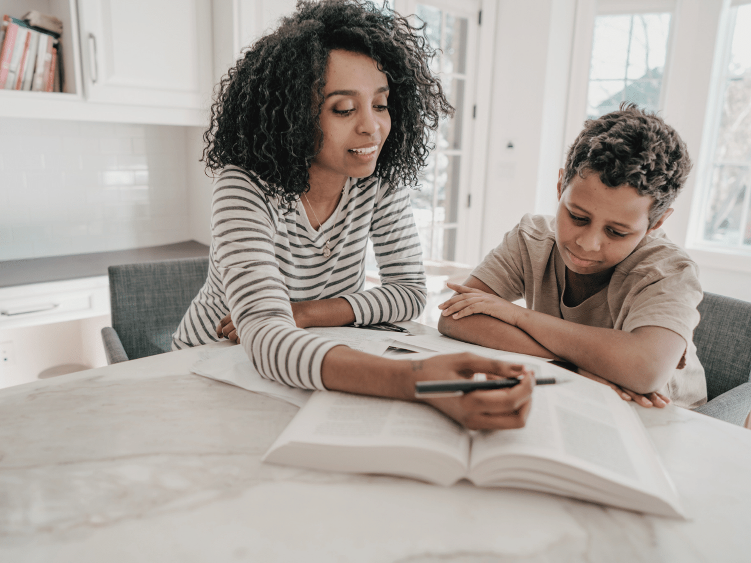 Parent and child reading a book together, holding a pen.