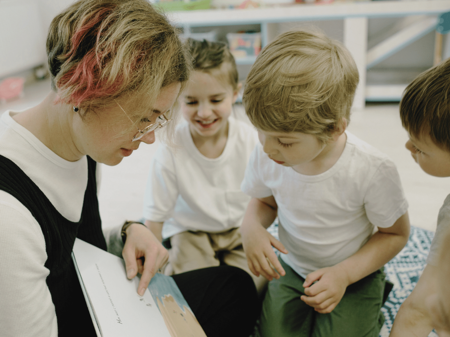 Someone reading to three children in a classroom setting.